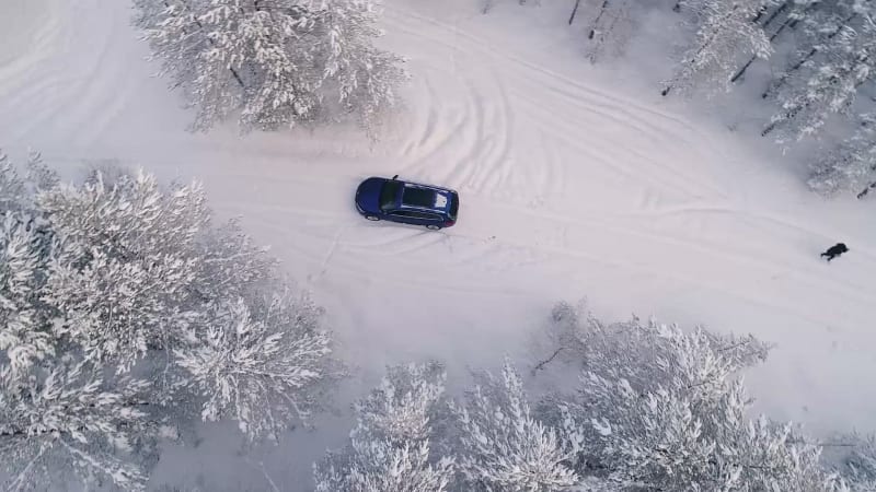 Aerial view of a car driving in the snowy forest.