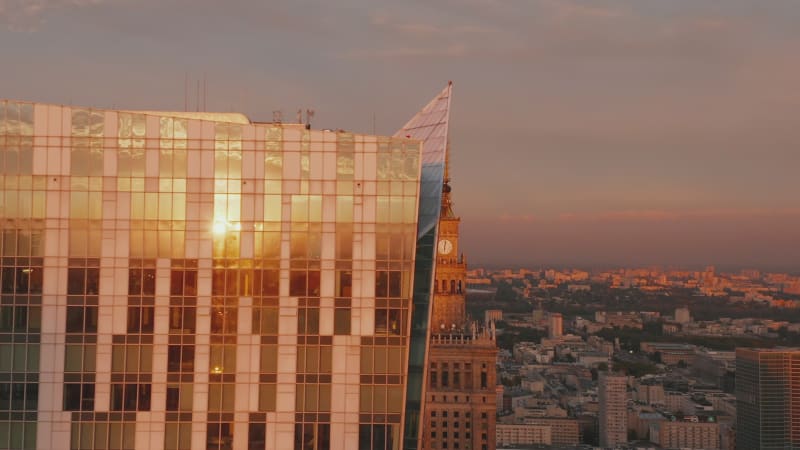 Slide and pan footage of modern building with glossy glass facade reflecting sunset sky. Revealing spire on top of PKIN building. Warsaw, Poland