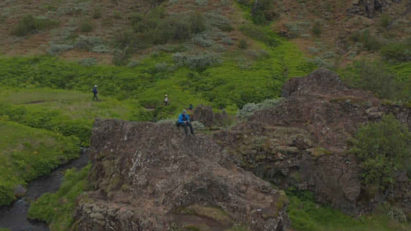 Drone view man sitting mountain peak in Iceland looking at amazing panorama feeling free. Aerial view tourist man hiker on top of rock formation meditating watching stunning icelandic landscape