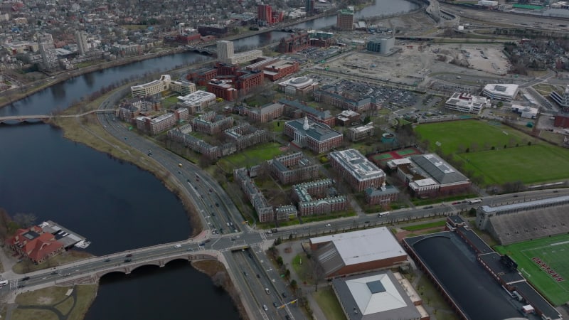 Aerial view of complex of classical red brick building on river waterfront. Harvard Business School site and busy road leading around. Boston, USA