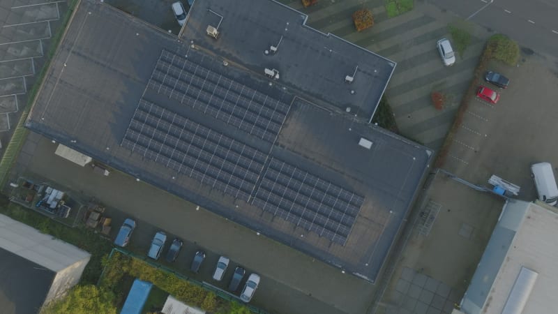 Top down turning zoom out shot of solar panels on industrial building roof in Alkmaar, The Netherlands, during sunrise.