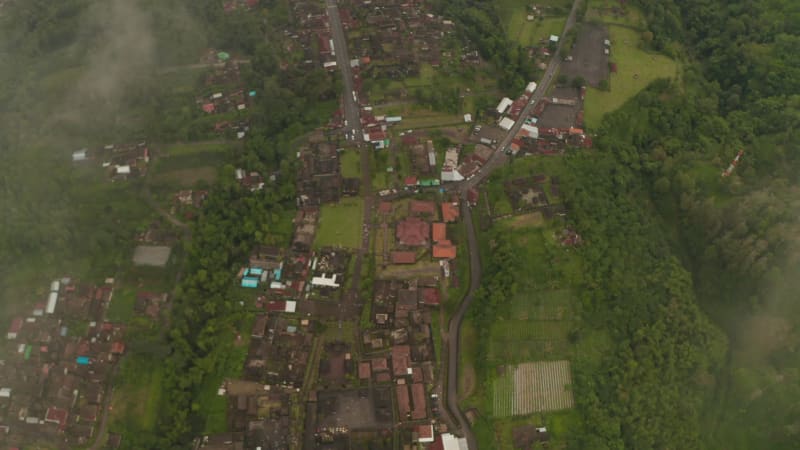 Flying through the clouds above Besakih Temple in Bali, Indonesia. Top down overhead aerial view of Besakih Temple surrounded by small village full of traditional Bali houses