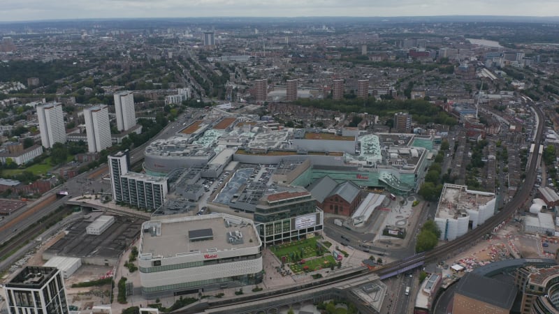 Aerial panoramic view of huge modern shopping mall. Urban neighbourhoods of large city in background. London, UK