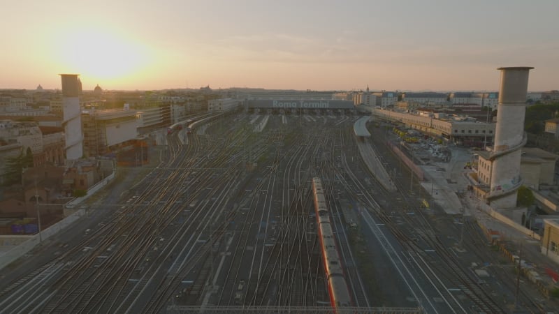 Fly over modern passenger train approaching Roma Termini train station. Aerial view against colourful sunset sky. Rome, Italy