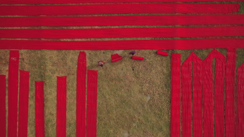 Aerial eines Mannes, der entlang roter langer Textilstreifen geht, Bangladesch.