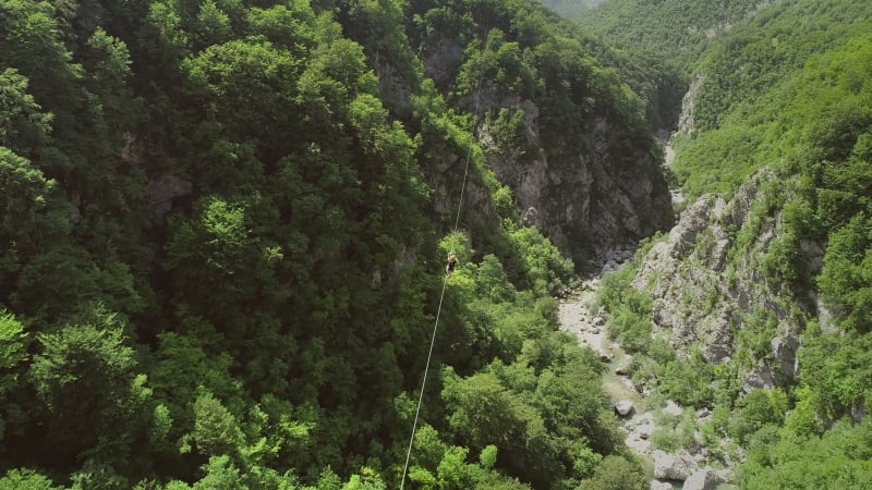 Aerial view of a person canopying over the forest in zip-line.