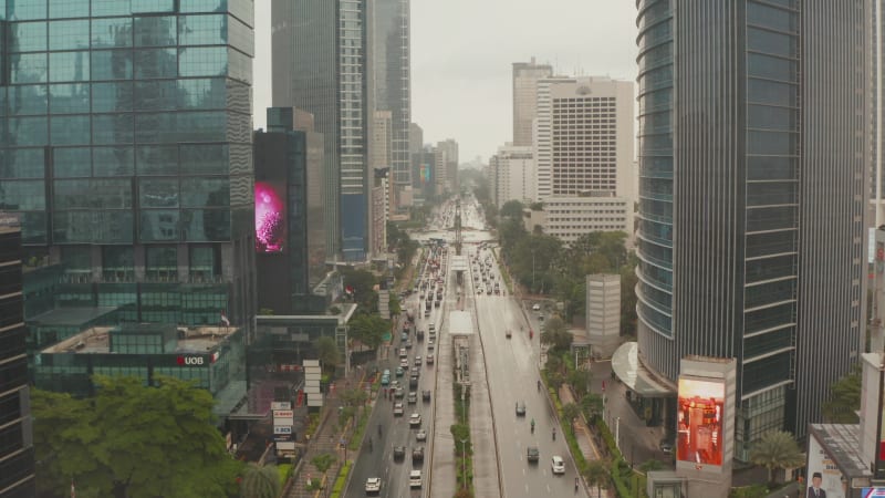 Ascending and descending aerial pedestal shot of multi lane traffic in urban city center between tall skyscrapers in Jakarta