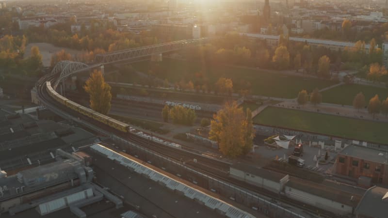 Subway Train from Aerial perspective passing bridge through public park in Berlin, Germany in Yellow and Orange autumn colors and Sunset golden light