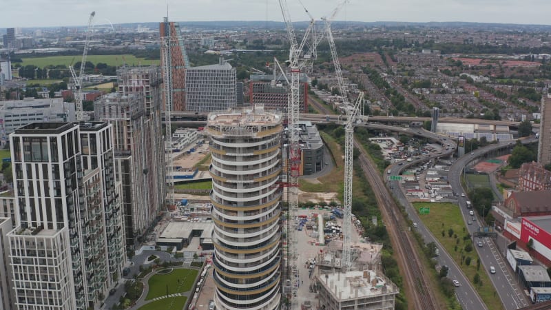 Tilt and pan shot of modern design tall building construction site. Tall tower cranes transporting material. New residential complex at White city borough. London, UK