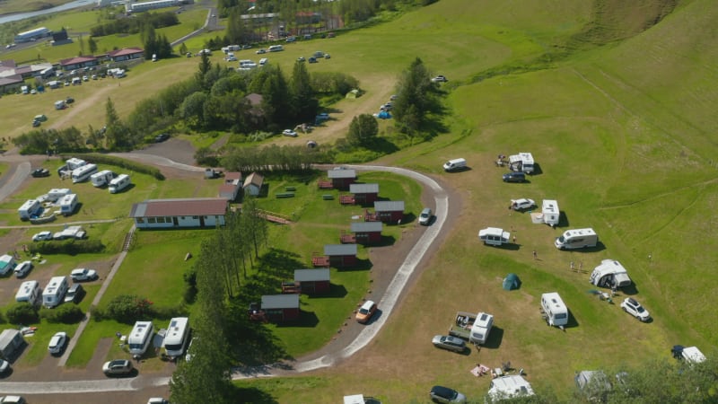 Directly above aerial view of campsite in green meadow highlands in Iceland. Top down view of characteristic wooden accommodation bungalow and tourist camping in motorhome