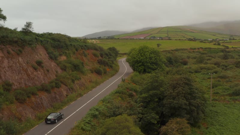 Forwards tracking of car driving on road winding through countryside. Cloudy and hazy weather. Ireland