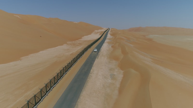 Aerial view of white car driving next to metal in the desert.