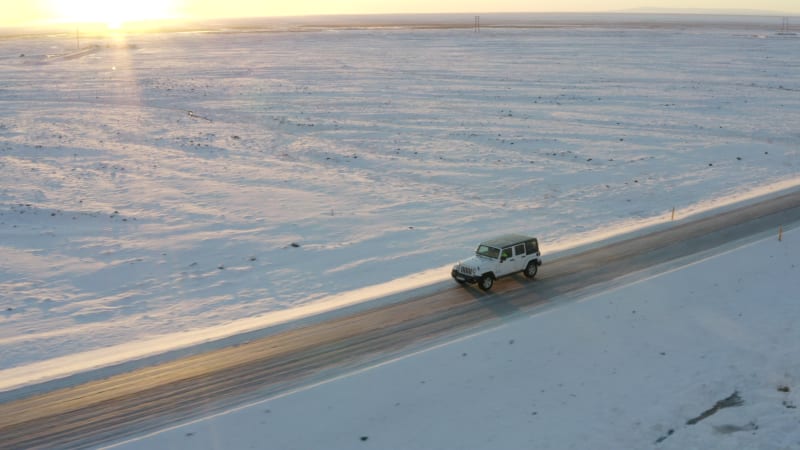 AERIAL: Flying besides Jeep on snowy road in Iceland at Sunset Winter, Sun, Arctic