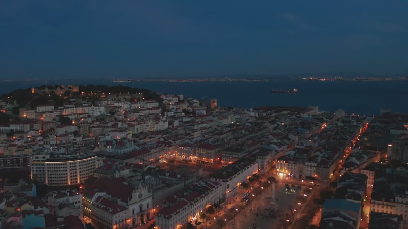 Aerial night view of urban city center of Lisbon with rows of traditional modern houses, castle on the hill and large public squares with lights