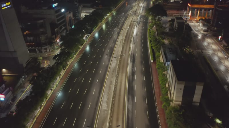 Low flying aerial tilting dolly shot of empty multi lane road in modern city center with skyscrapers at night