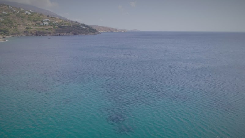 Aerial view of calm sea waters with small hill and houses at the end.