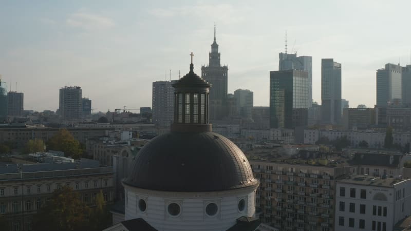 Fly around dome of Holy Trinity Church with golden cross on top. Cityscape with high rise buildings in background. Warsaw, Poland