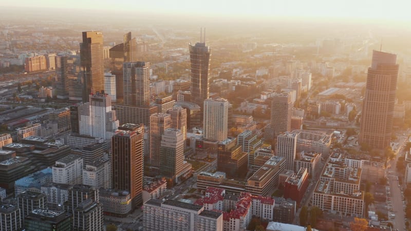 Slide and pan aerial panoramic footage of modern downtown buildings in morning sun glow. Warsaw, Poland