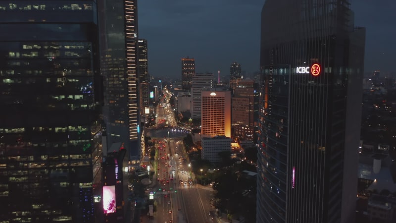 Aerial dolly shot descending towards night time traffic on Selamat Datang Monument roundabout in Jakarta, Indonesia