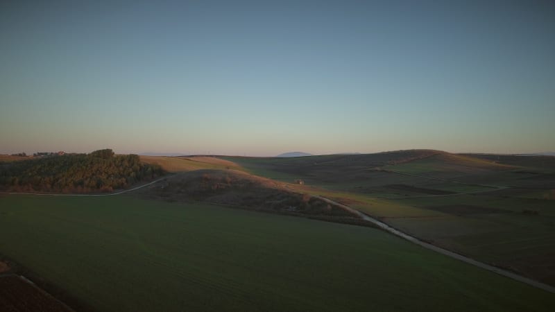 Aerial view of beautiful hills with lots of grass and trees at sunset.