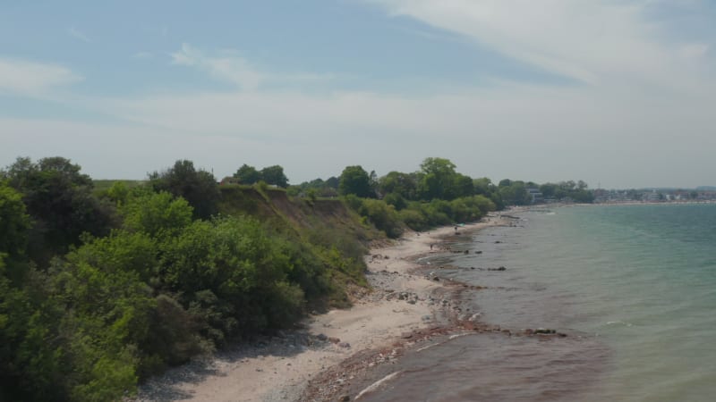 Low aerial drone view of Brodten shoreline by countryside green fields, Germany, forward, day