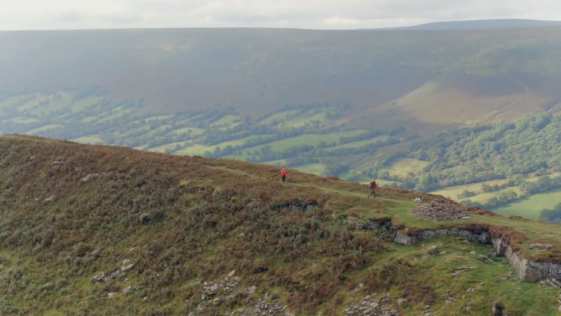 Two People Walking a Dog in a Hilly and Mountainous Landscape