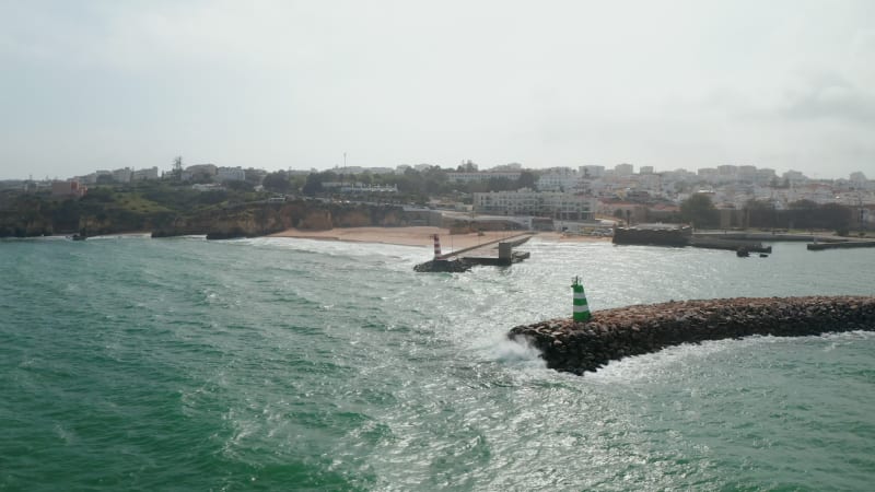 Majestic aerial view of waves breaking against breakwater structure in Lagos, Portugal, flying forward, day