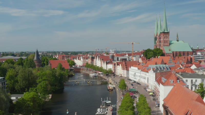 Forwards descending footage of Trave waterfront with moored boats, restaurant terraces and people walking along river. Historic city centre. Luebeck, Schleswig-Holstein, Germany