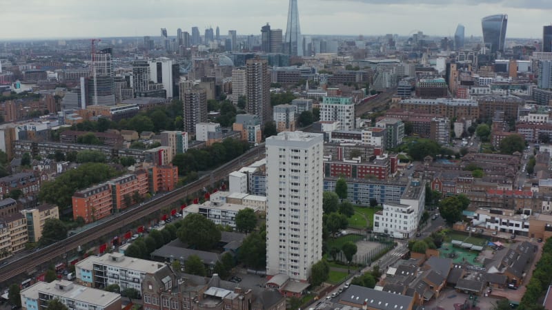 Forwards fly above urban neighbourhood. Tilt up reveal cityscape with skyscrapers on horizon. London, UK