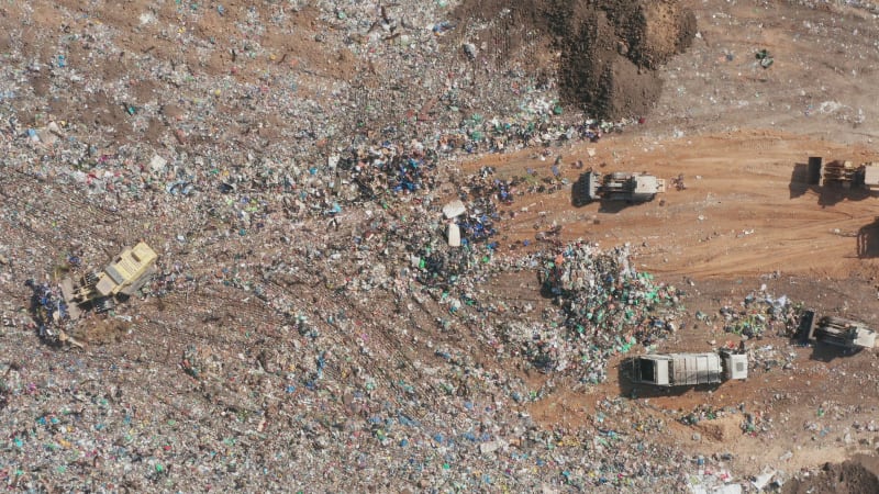 Top down aerial footage of a Municipal Solid waste Landfill during collecting, sorting and pressing work, with a massive flock of birds.