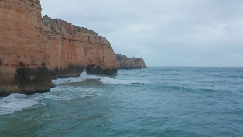 Scenic background banner aerial drone view of Lagos coastline with waves crashing against cliffs on cloudy day, Portugal