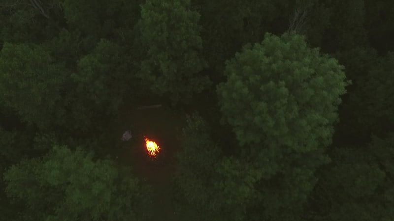 Aerial view of friend eating close to campfire in forest.