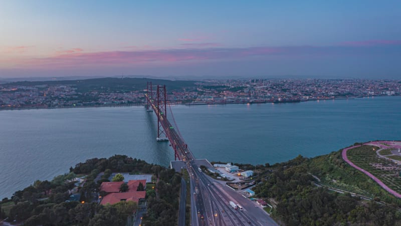 Aerial day to night hyperlapse of beautiful Lisbon cityscape with Ponte 25 de Abril red bridge and Sanctuary of Christ the King by the sea