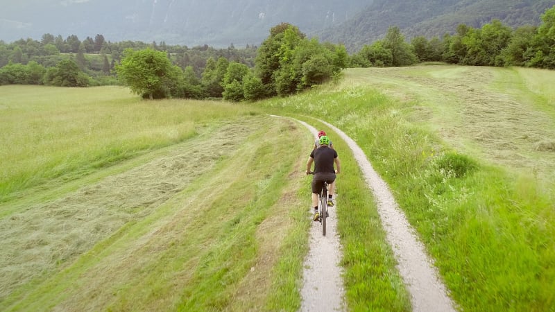 Aerial view of two cyclists riding bike in the forest on dirt road.