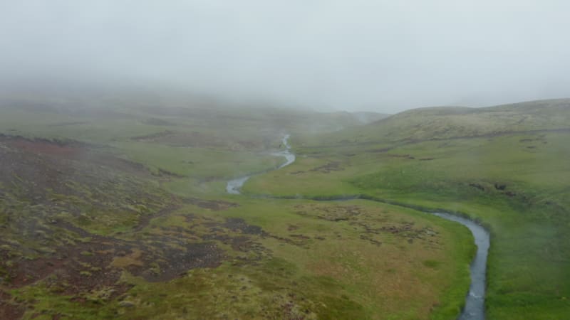 Birds eye view of Reykjadalur hot spring river pools valley in foggy day. Misty drone view of geothermal hot river streaming in Iceland green countryside