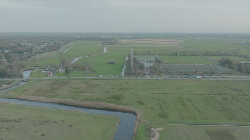 Flying forwards turning towards a dutch football club near green farmer fields and water next to the village Bergen in The Netherlands at cloudy daytime.