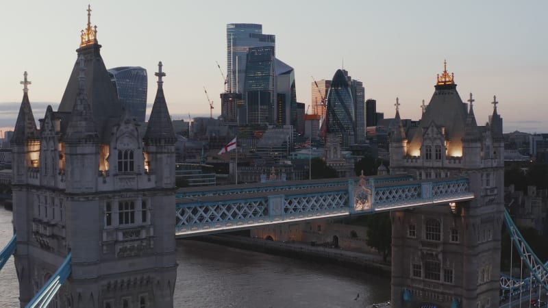 Low flight above top walkway on Tower Bridge in evening. Heading to group of skyscrapers with glass facades. London, UK