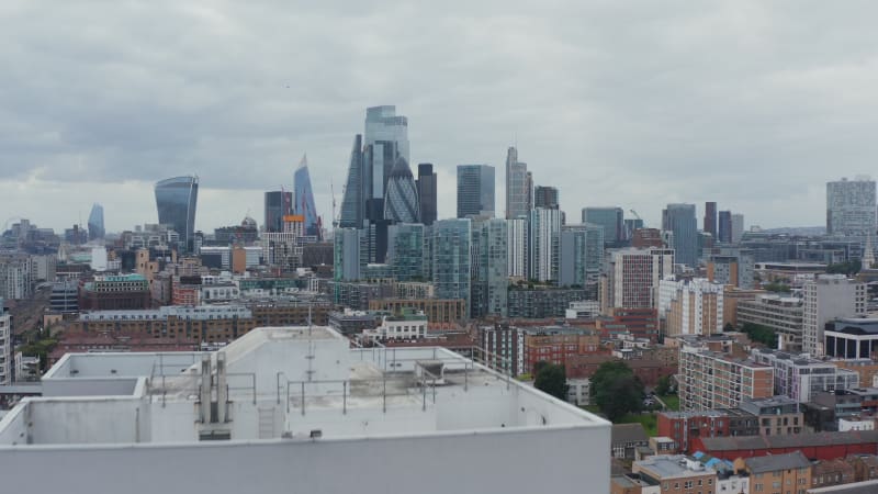 Forwards fly over top of tall building. Panoramic view of iconic skyscrapers in City business hub. London, UK