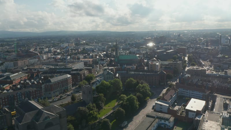 Fly above city, view against bright clouds and sunshine. Town development and public parks. Dublin, Ireland