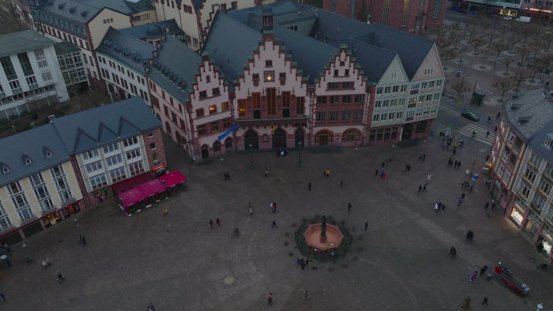 High angle view of historic square. Fountain and medieval houses around Roemerberg. Tilt up reveal of group of modern downtown skyscrapers. Frankfurt am Main, Germany