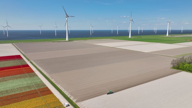 Aerial 5K view of farmland with tractor and wind farm, Flevoland, Netherlands.