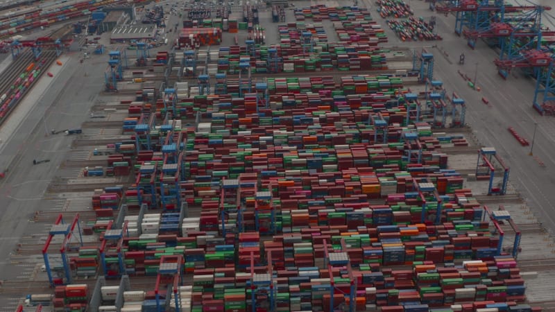 Aerial view of rows of colorful cargo containers in large industrial port being moved by automated cranes