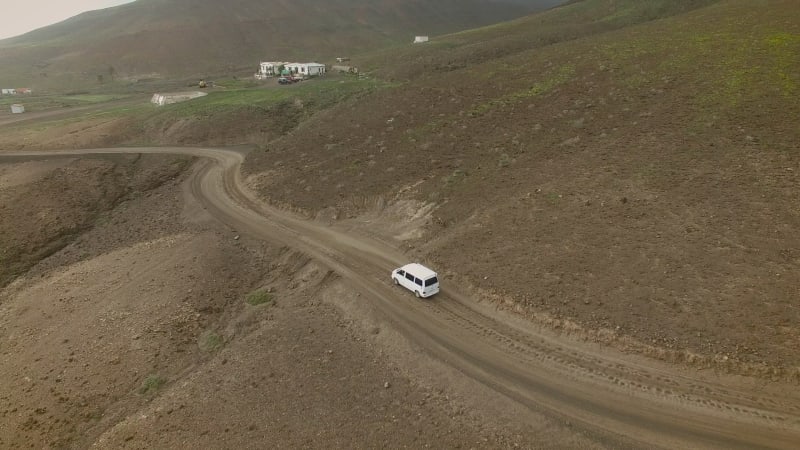 Aerial view of a family van car on a curvy and dirt road.