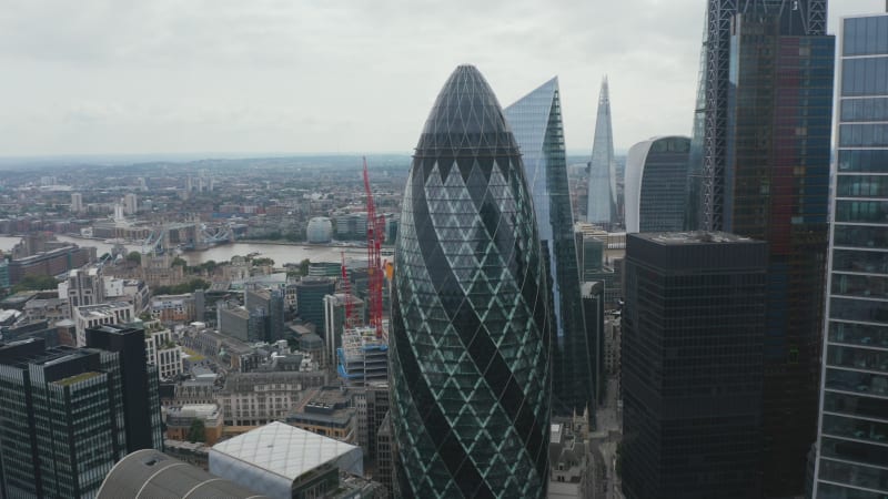 Elevated view of Gherkin skyscraper. Backwards reveal of group of modern tall office buildings in City financial hub. London, UK