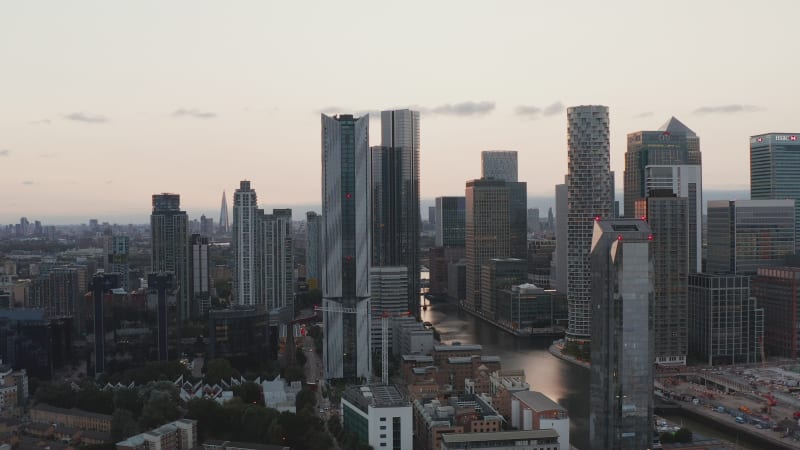 Slide and pan footage of modern tall buildings along South dock water channel in sunset time. Futuristic Canary Wharf financial hub. London, UK