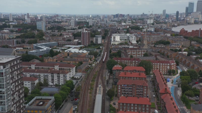 Forwards tracking of trains driving side by side on railway line in city. Aerial panoramic view of urban neighbourhood. London, UK