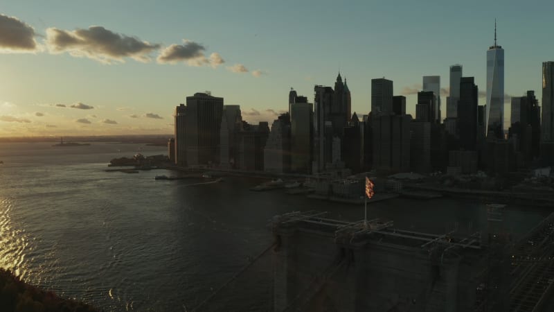 Breath taking aerial footage of colourful sunset sky above water. Silhouettes of Brooklyn Bridge and downtown skyscrapers. Manhattan, New York City, USA