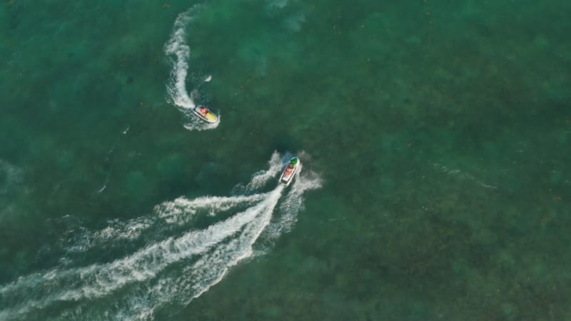 Jet ski riders enjoying their time while cruising on the calm sea surface. Aerial Birds Eye Overhead Top Down View, rotating counterclockwise