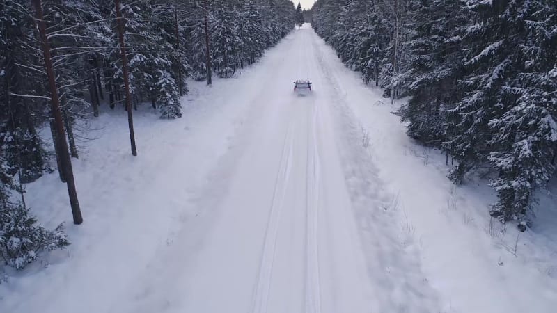 Aerial view of a car driving in the snowy forest.