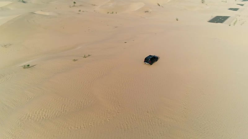 Aerial view of black car driving on road covered by sand.